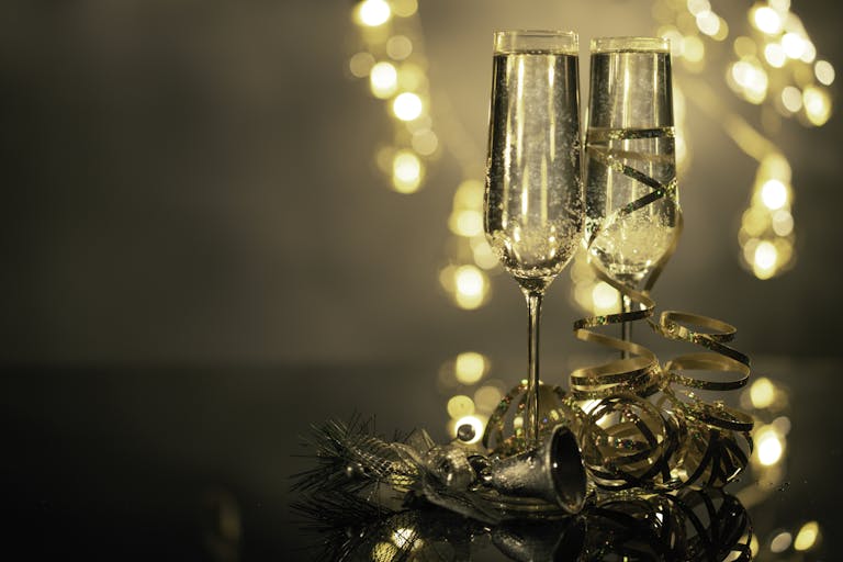 Champagne glasses with ribbons against festive bokeh lights.