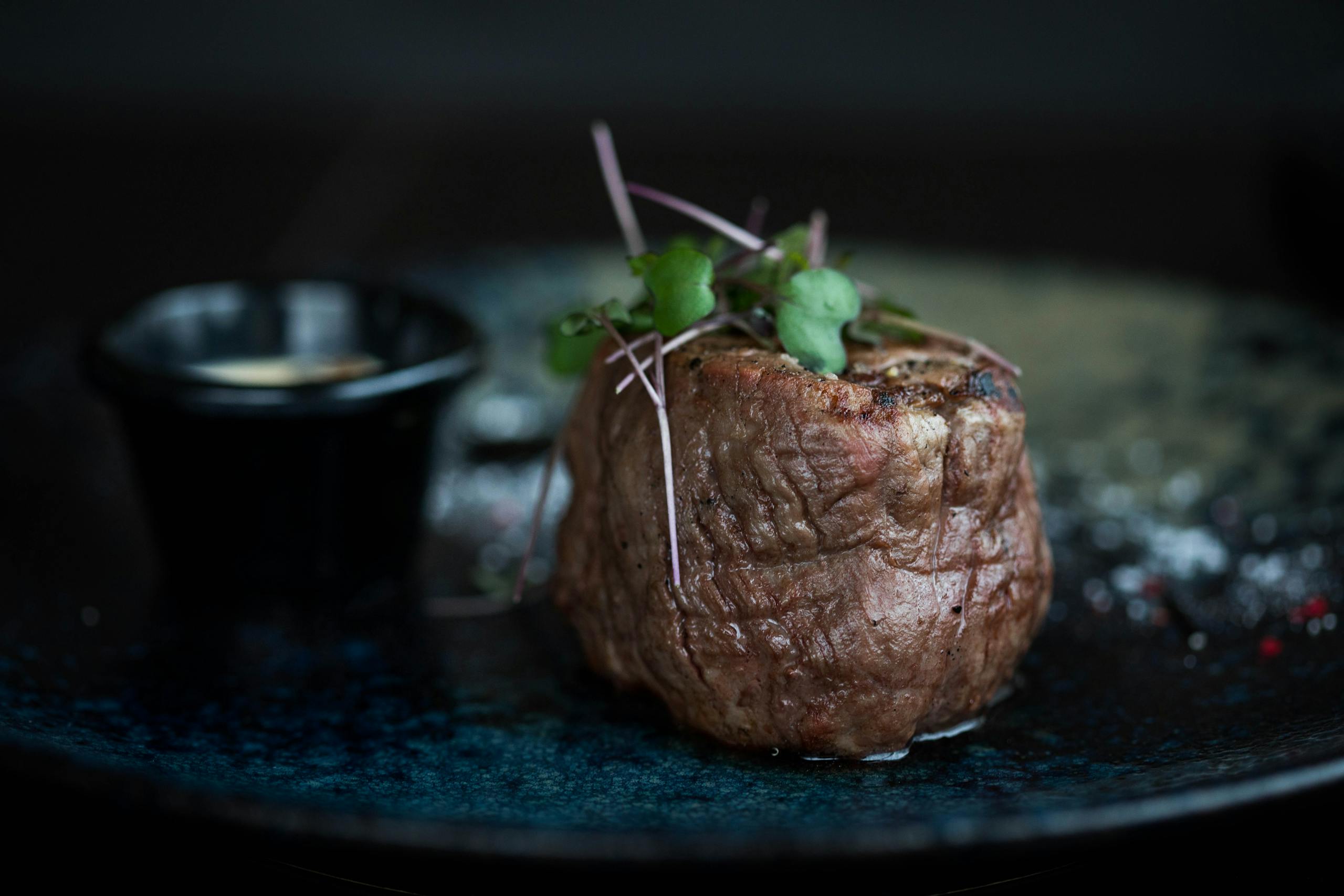 Succulent grilled steak topped with microgreens served on a dark plate for a gourmet meal.